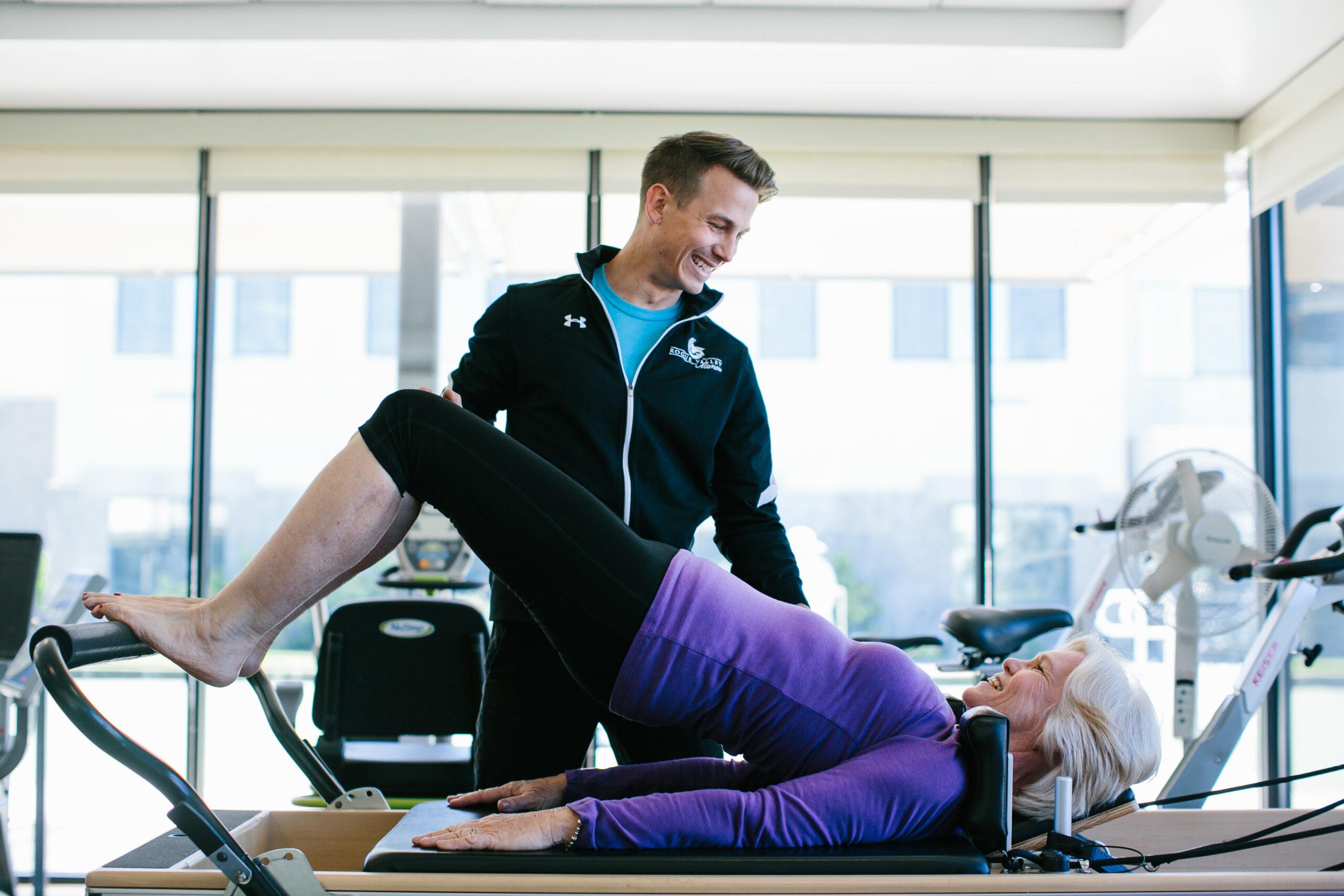 A personal trainer works with an older woman on a stretching exercise.