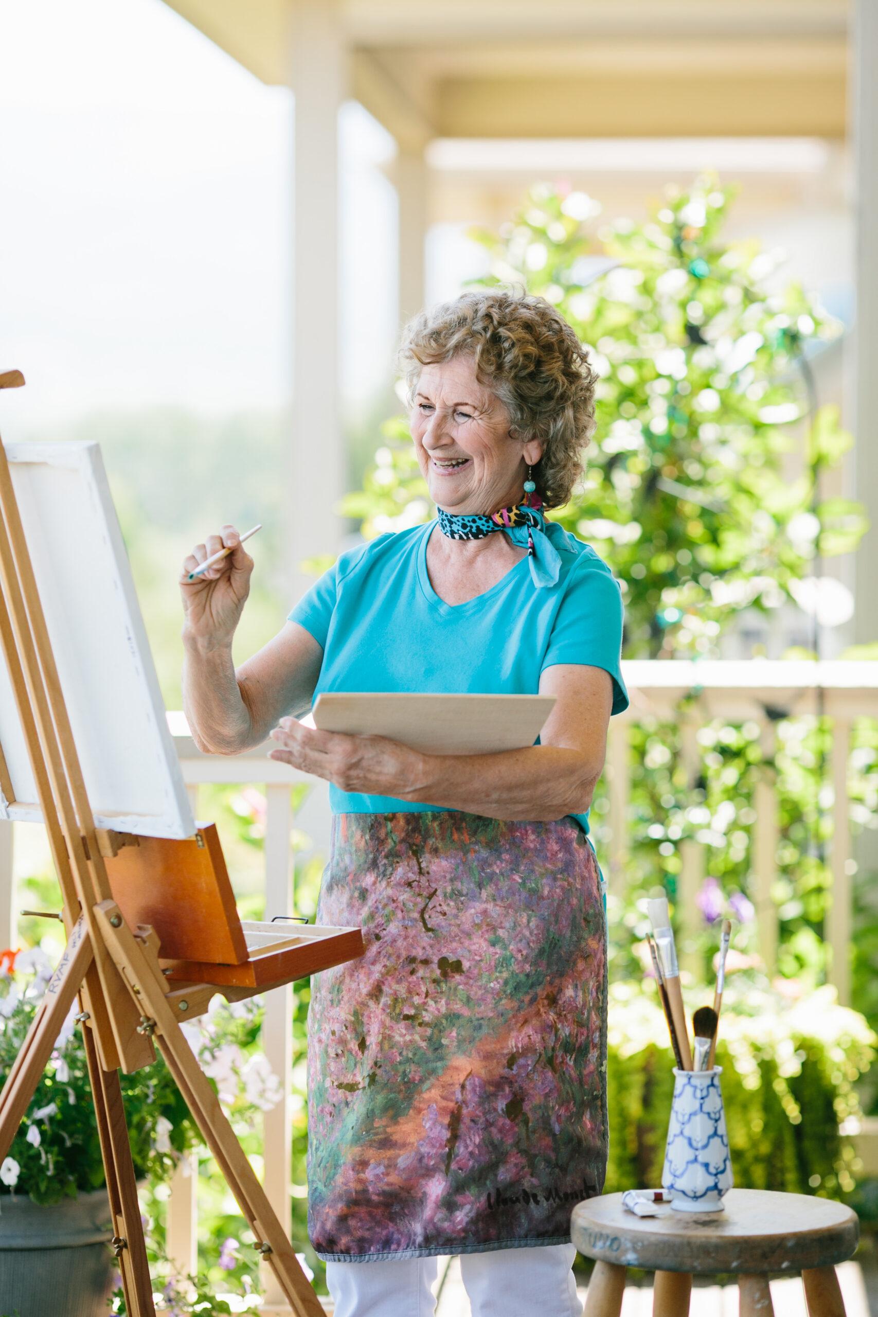 A happy woman wearing vibrant blue accessories paints on a canvas.