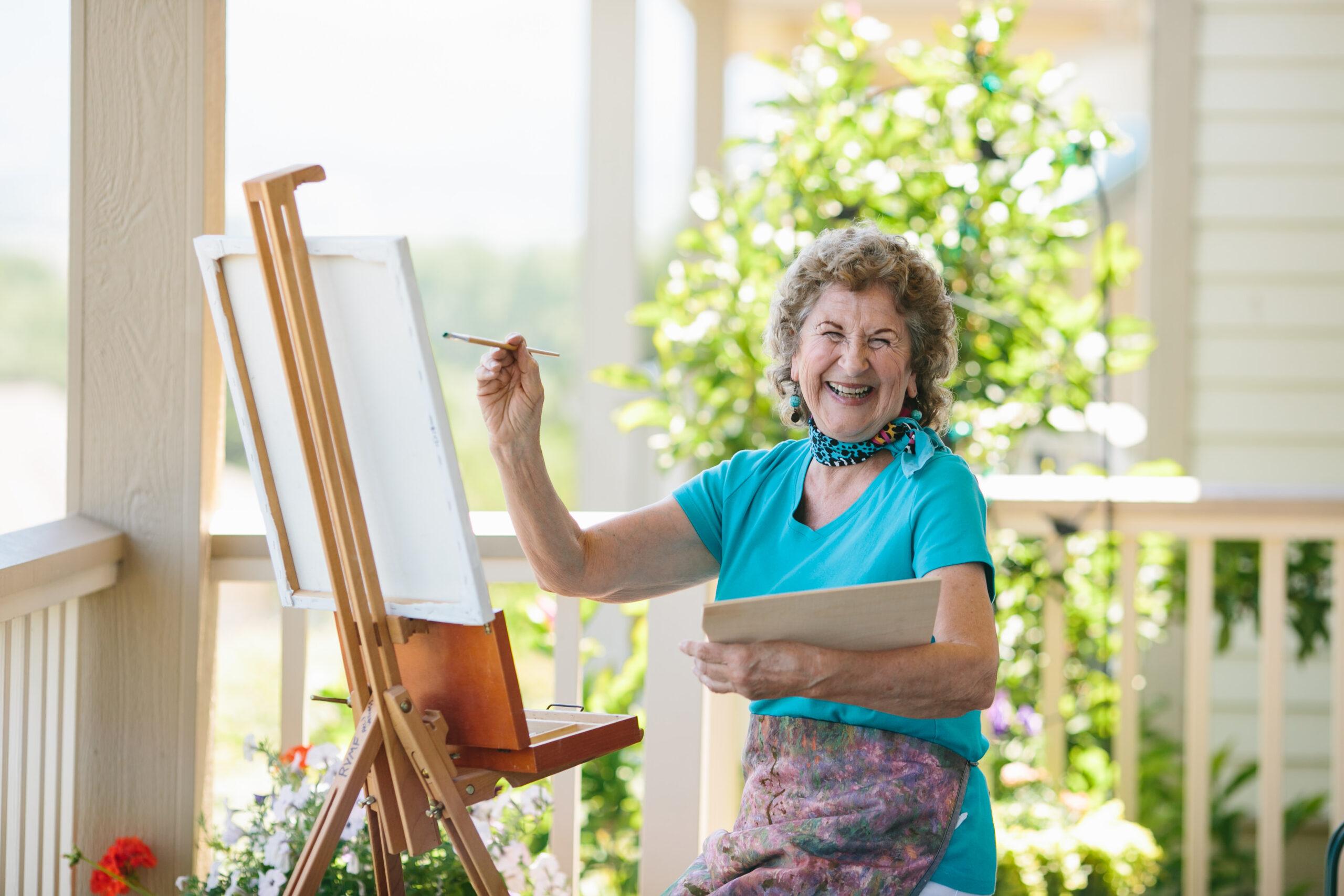 A happy woman wearing vibrant blue accessories paints on a canvas.