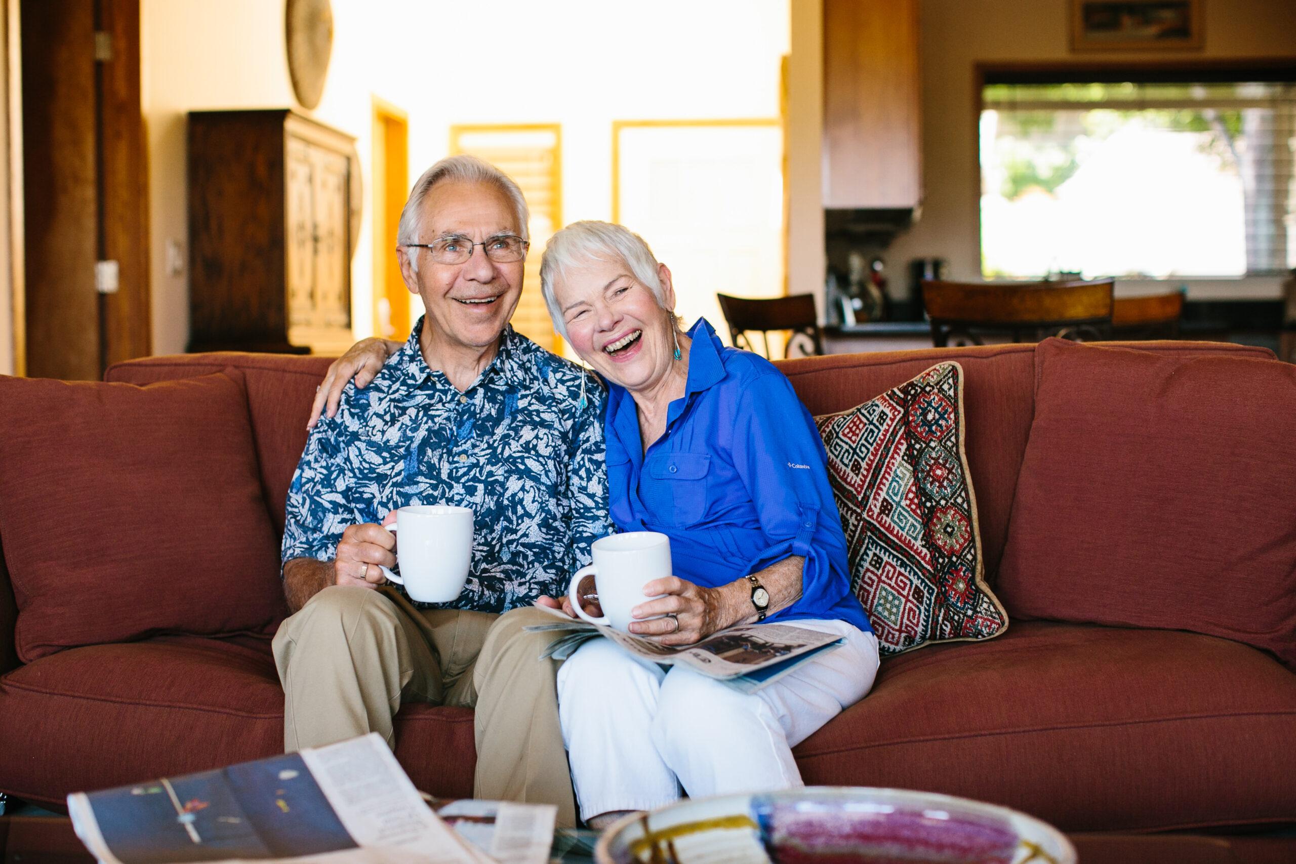 A happy couple sits on a couch, holding coffee cups.