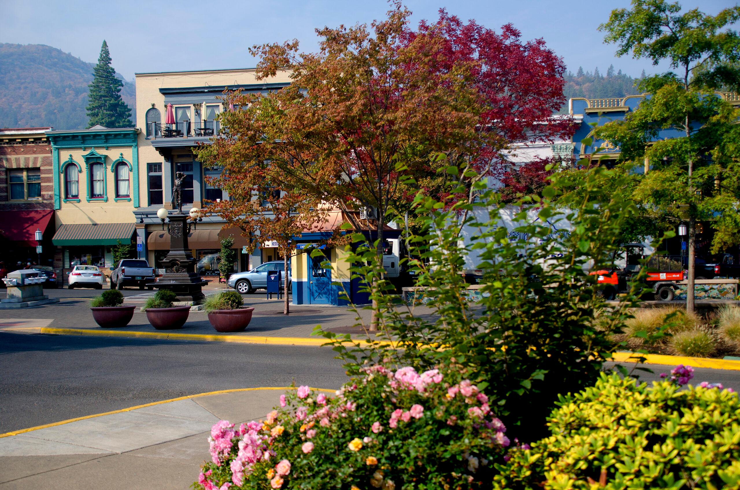 Downtown Ashland. There is foliage, brightly-colored buildings and mountains in the background.