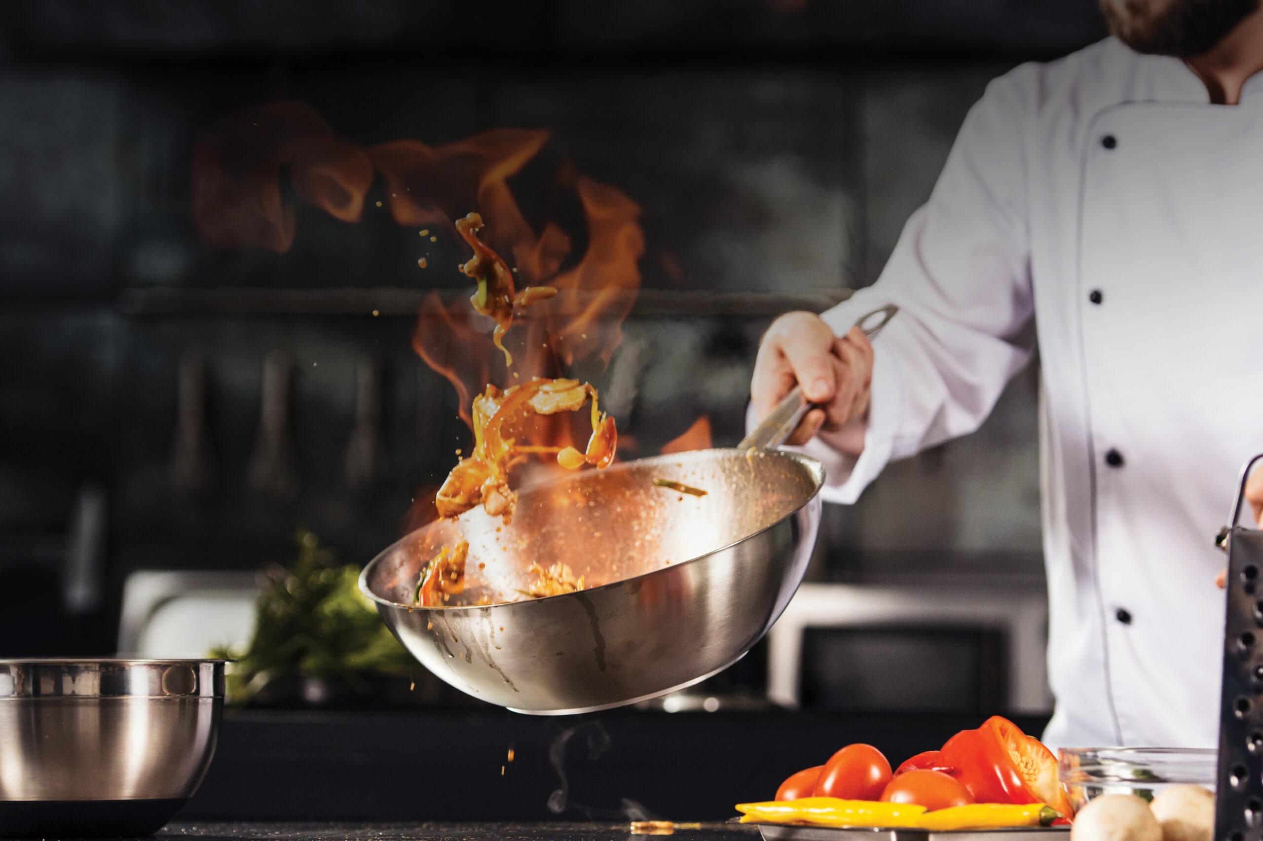 Closeup photo of a chef using a wok. The ingredients are on fire as the chef stir fries them.