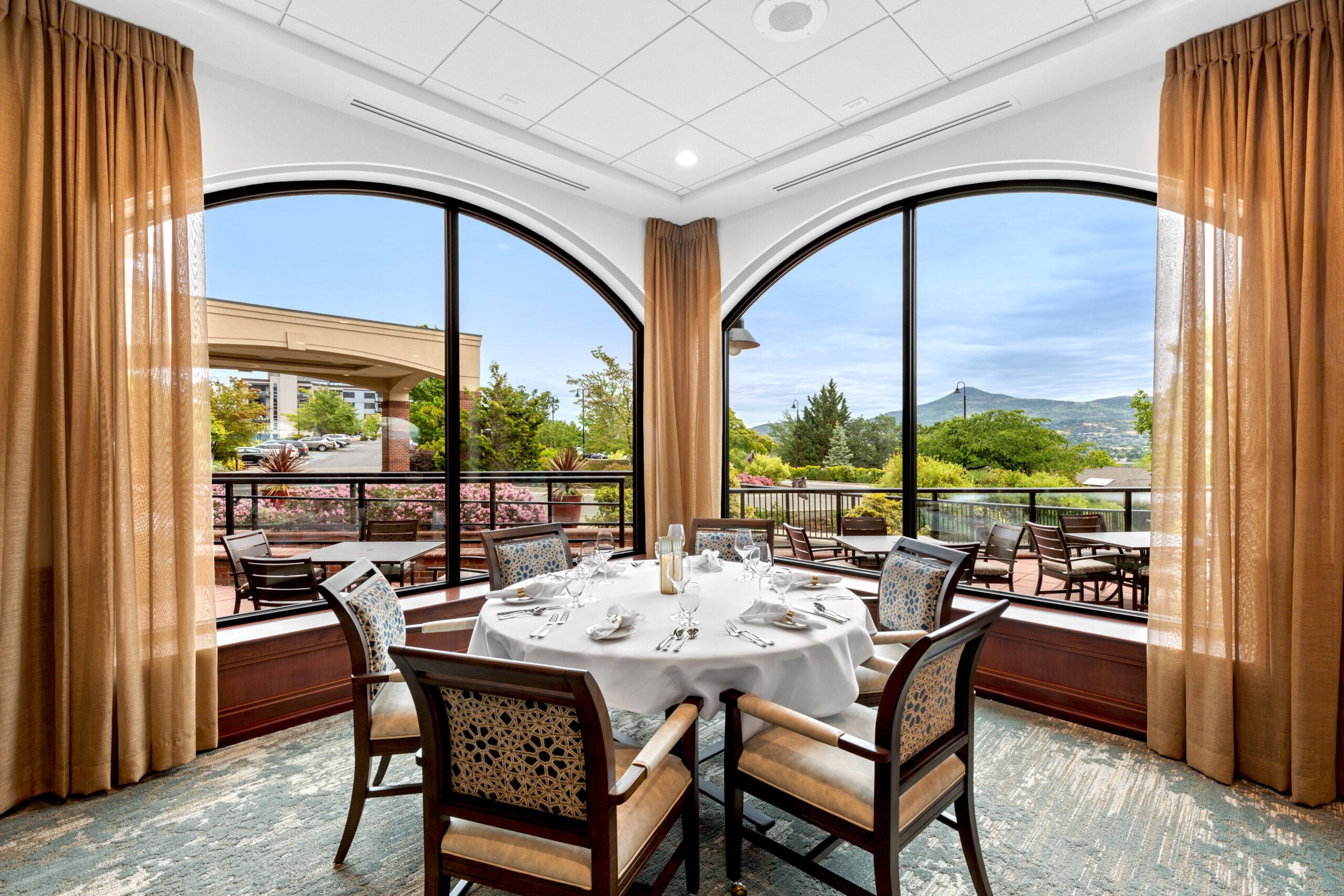 A formal dining room surrounded by windows at Rogue Valley Manor.