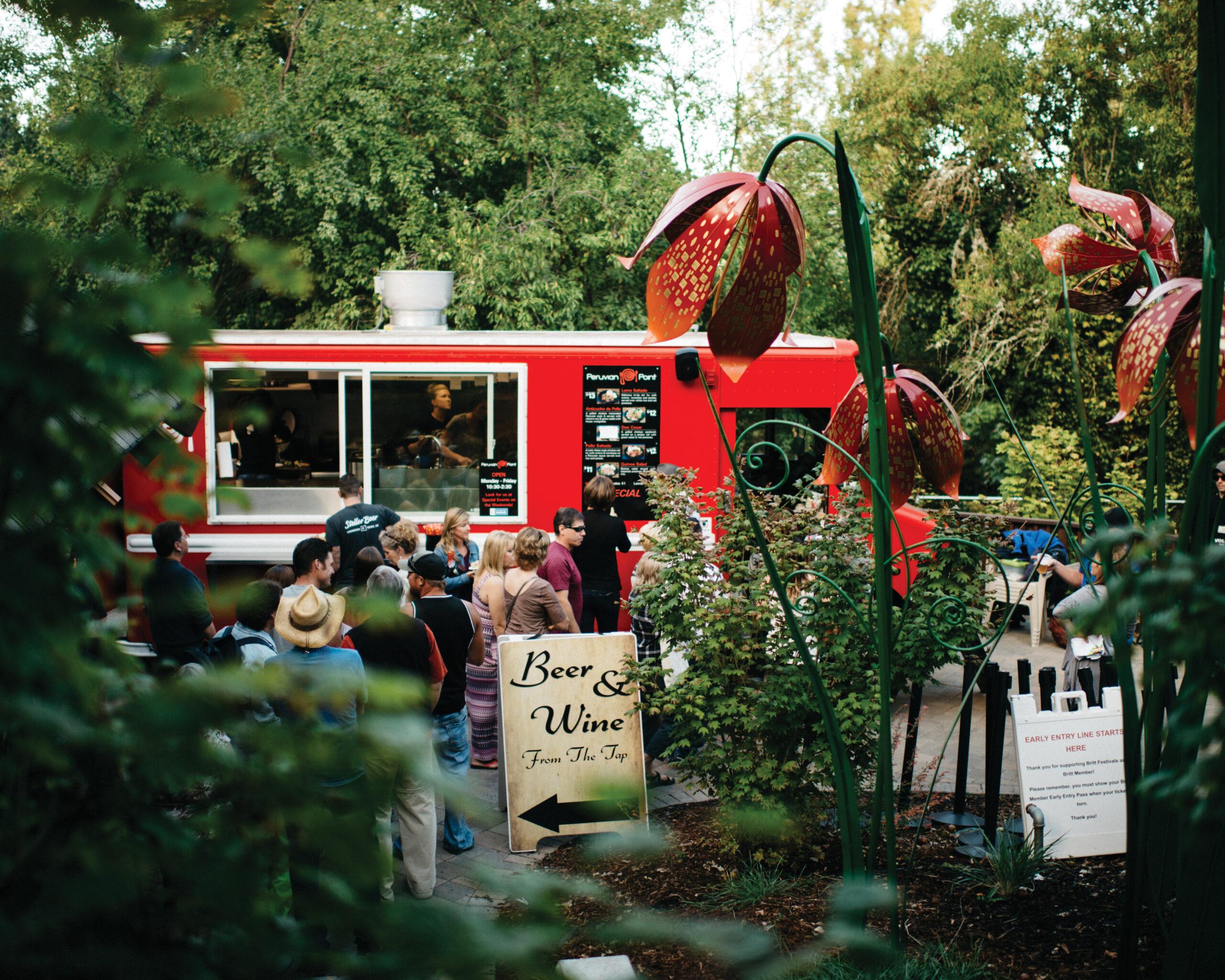 A line forms in front of a red food truck selling Peruvian food. There is a sign reading Beer and Wine from the tap in front of the truck.