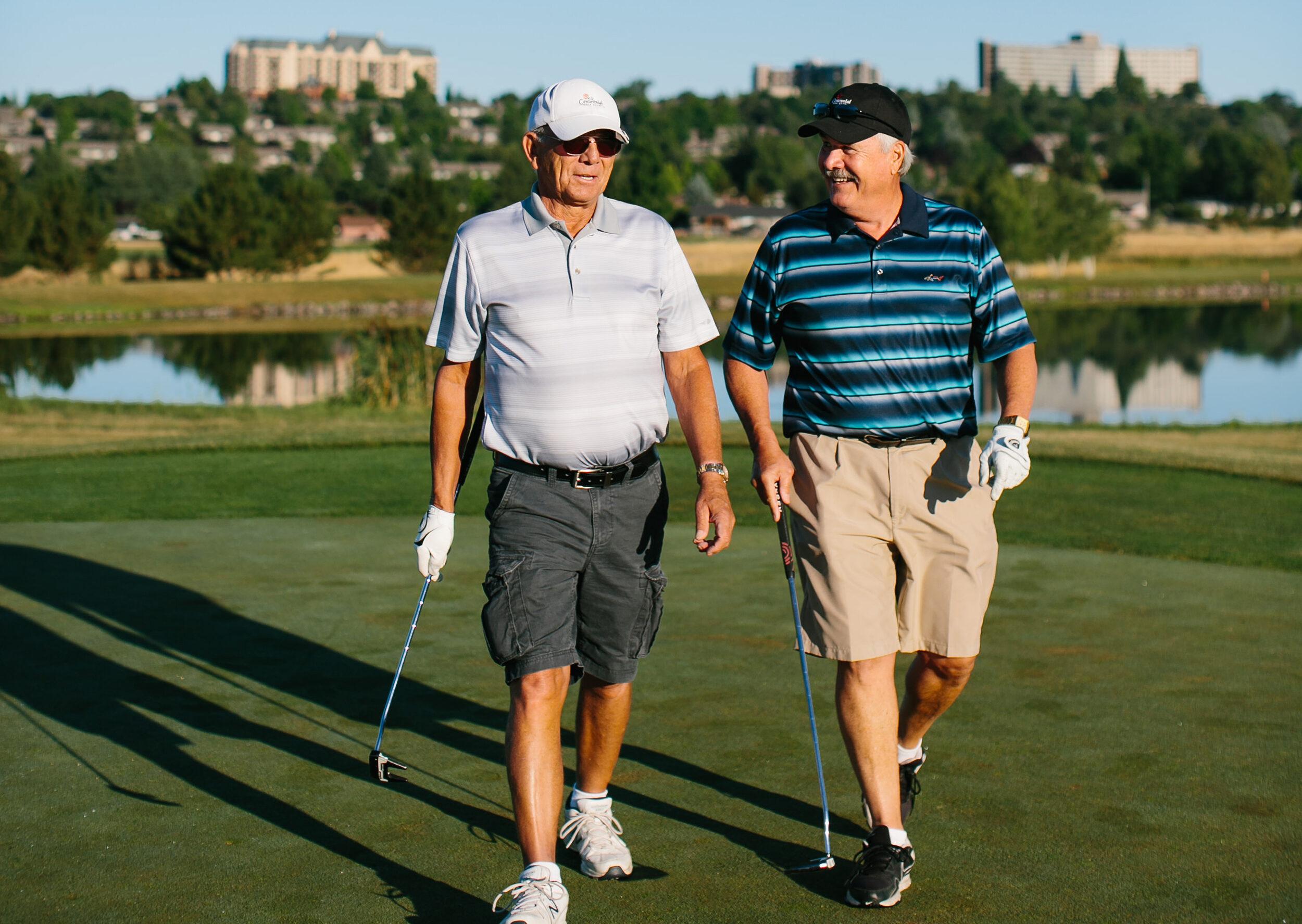 Two friends walk and talk on a golf course.