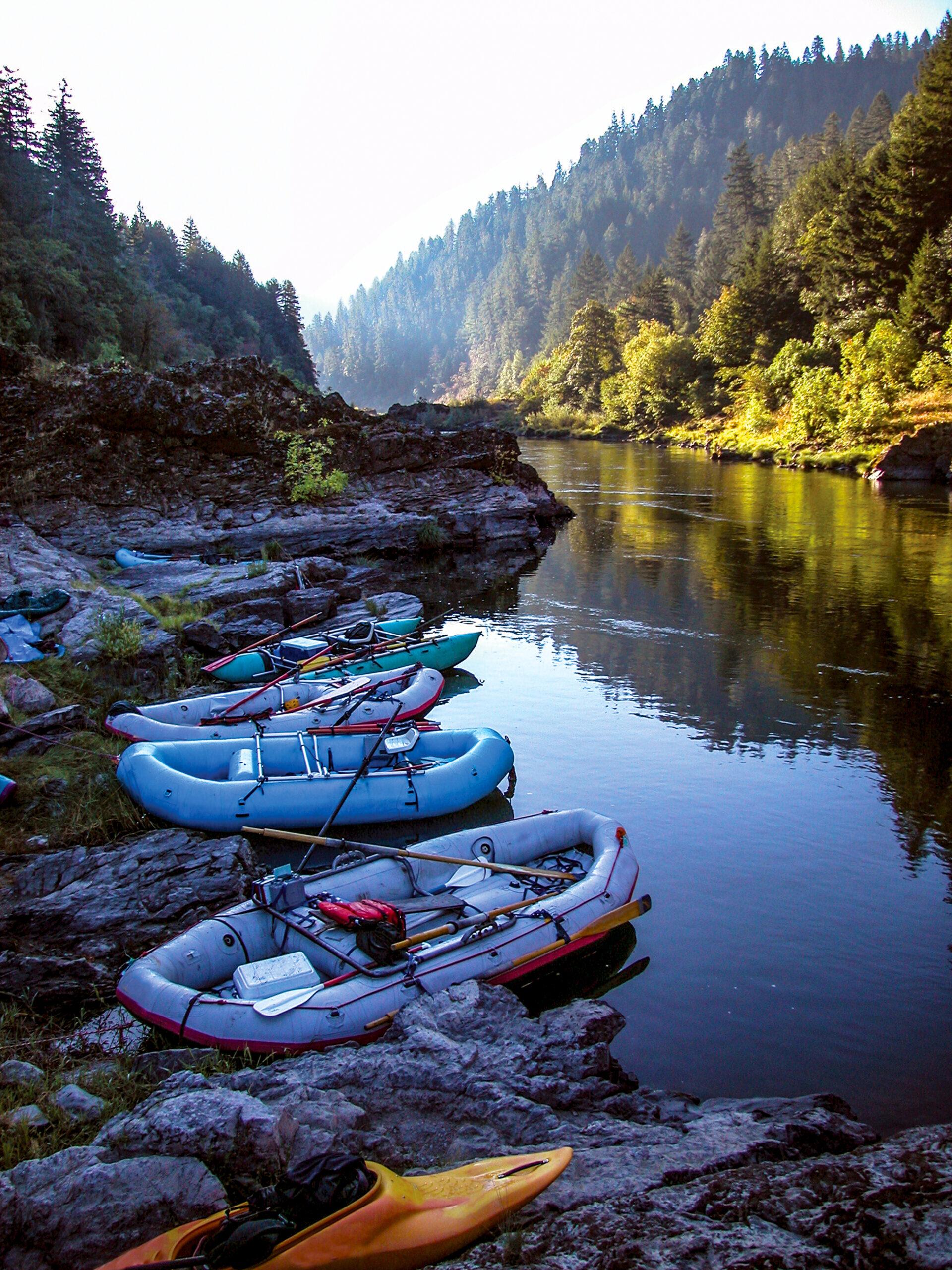 Empty river rafts in a picturesque river lined with pine trees.