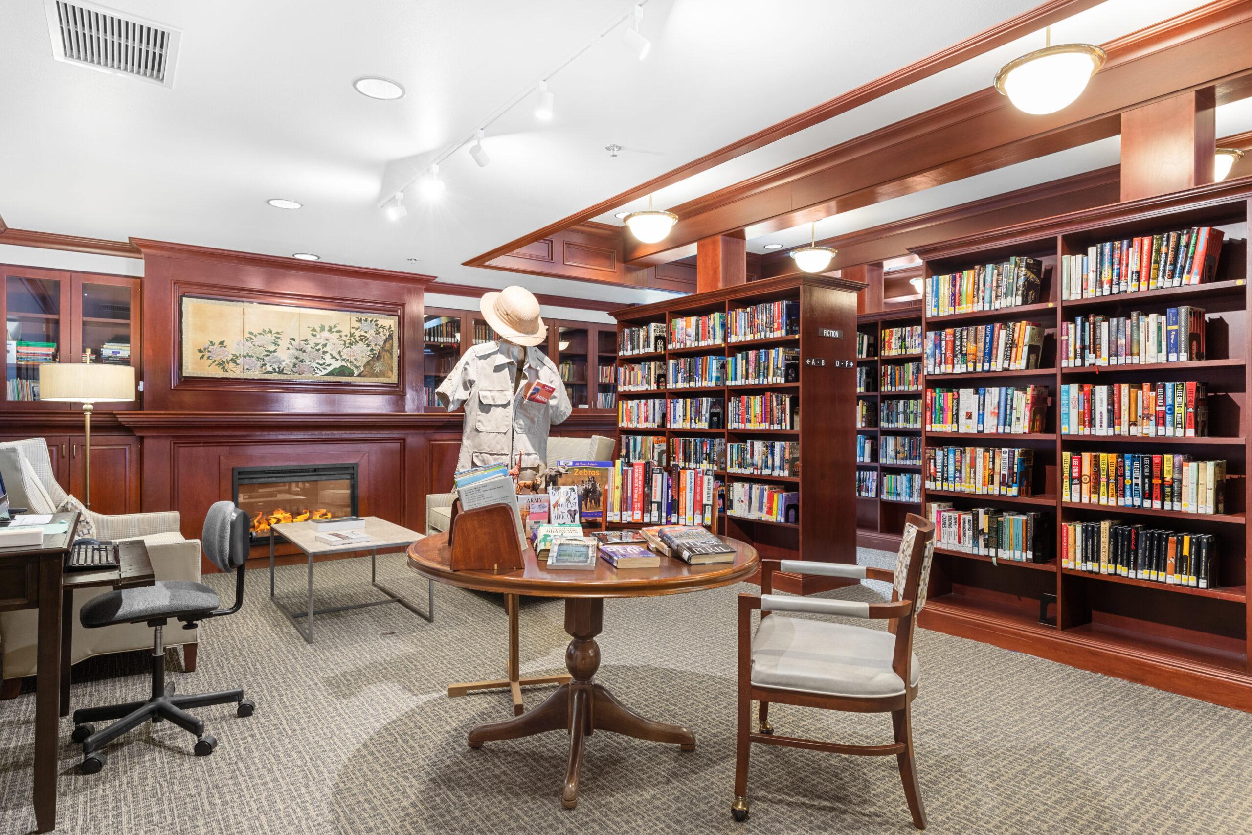 A library with various shelves of books and a computer area. There is a display of a mannequin wearing safari clothes and reading a book.